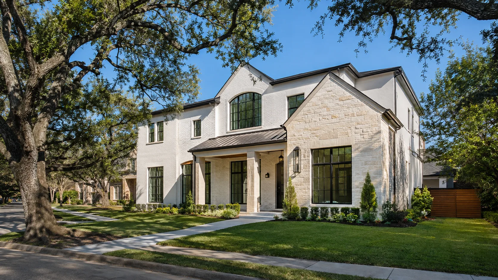 A two-story custom home on a tree-lined residential street in Bellaire, Texas, with a clipped lawn and mature oaks, photographed on a clear afternoon