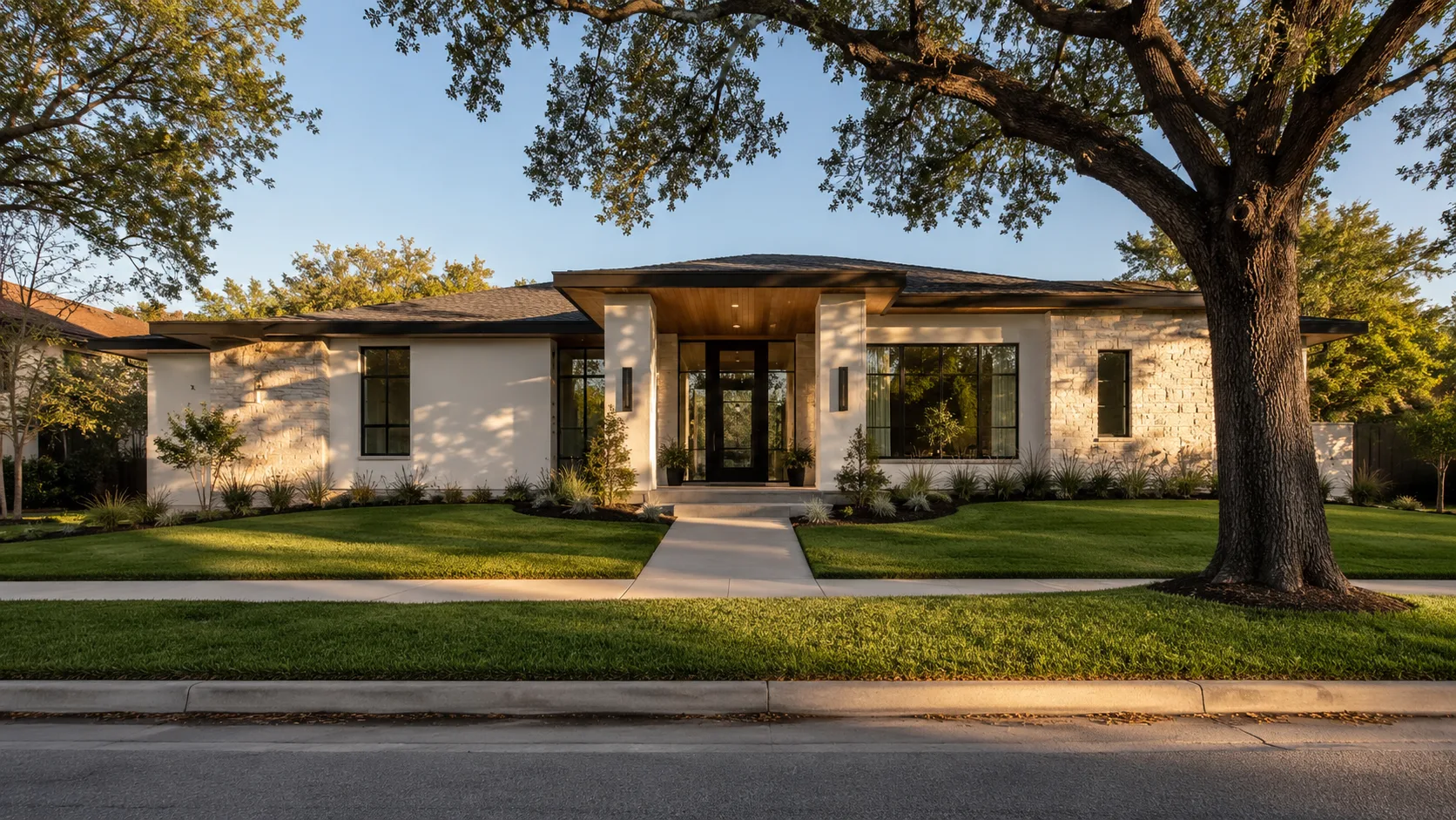A single-storey modern house set back behind a clipped front lawn on a Houston residential street, with a concrete walk, a grass verge and a curbside oak in the foreground